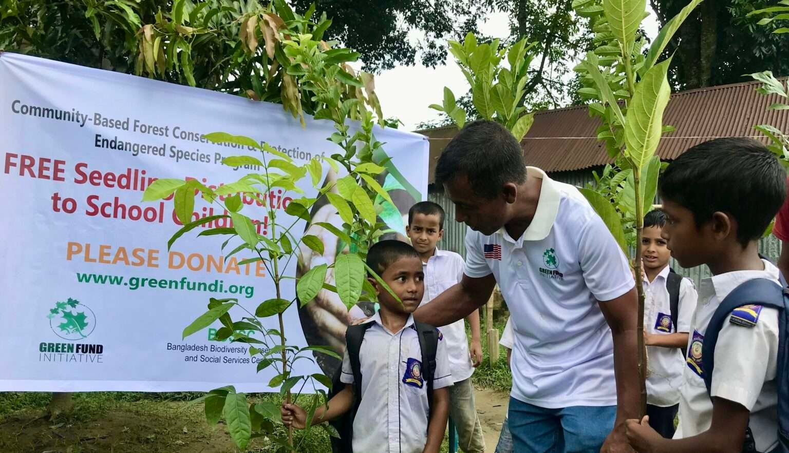 A GFI volunteer handing free tree seedlings to schoolchildren