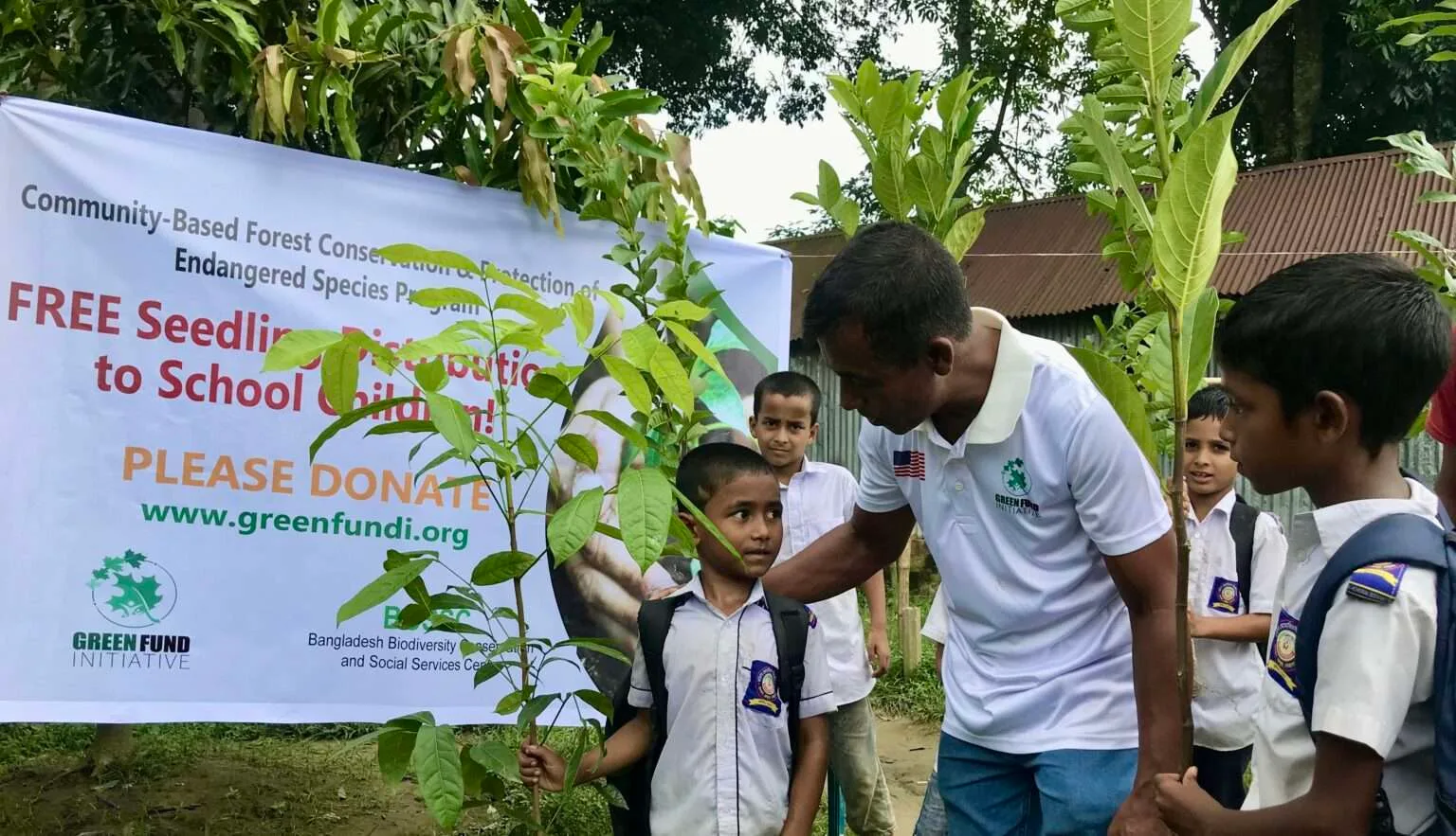 A GFI volunteer handing free tree seedlings to schoolchildren