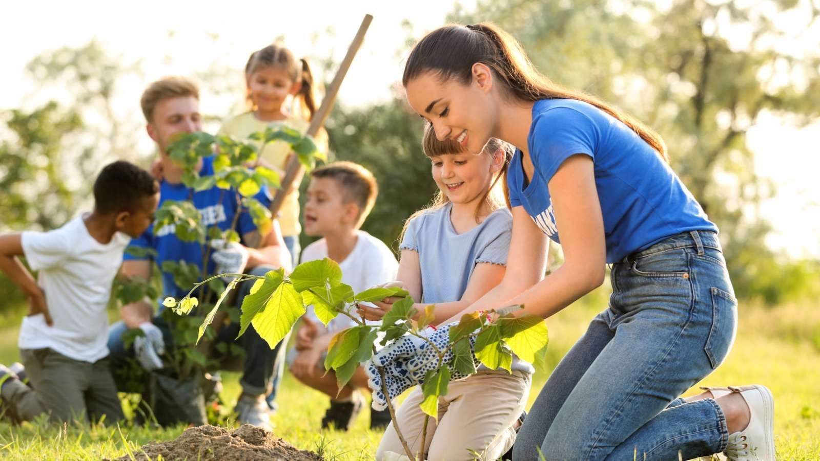 A young woman and a group of children planting a tree together