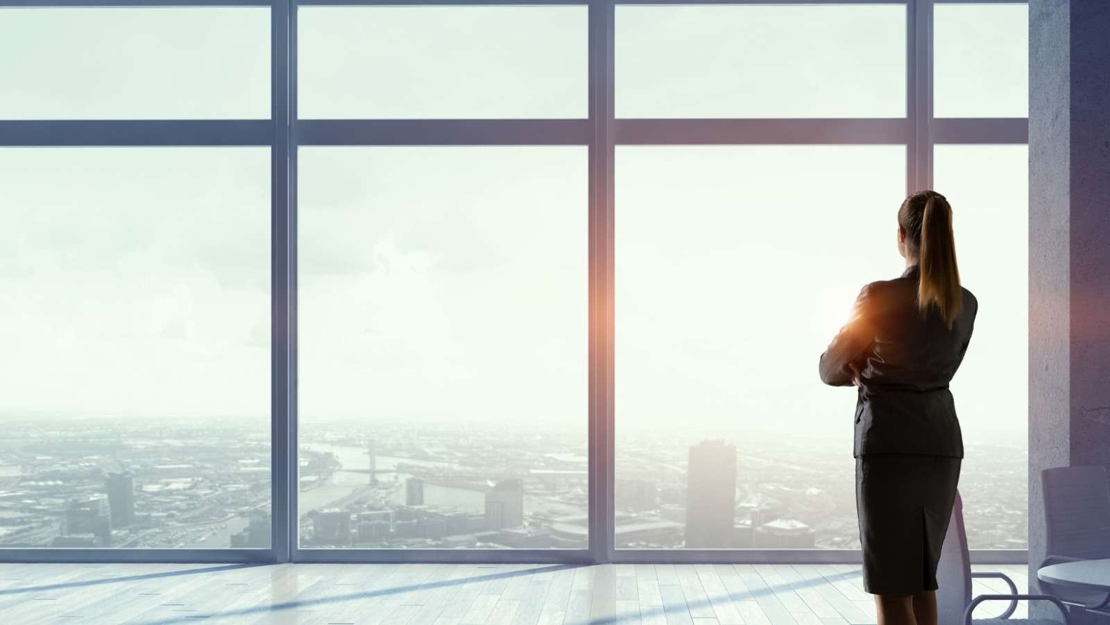 A person standing at a tall office window looking out over a city