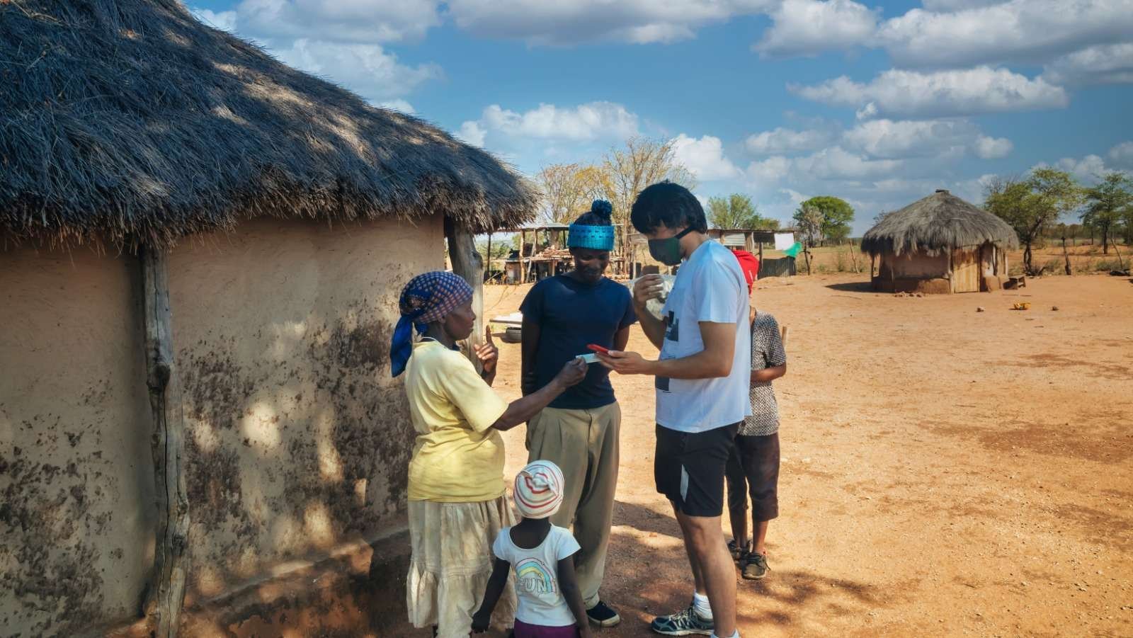 Aid workers talking with a family outside a thatched house in a rural village
