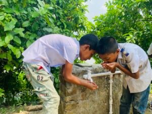 Two schoolchildren drinking water from the newly installed water facility at a rural school in Netrokona, Bangladesh.