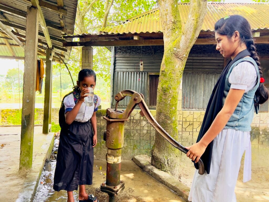 Schoolchildren collecting water from the existing hand pump before the water tank project in rural Netrokona.