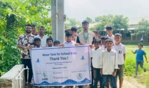 Students and project representatives holding a thank-you banner beside the newly installed water facility in Netrokona, Bangladesh.